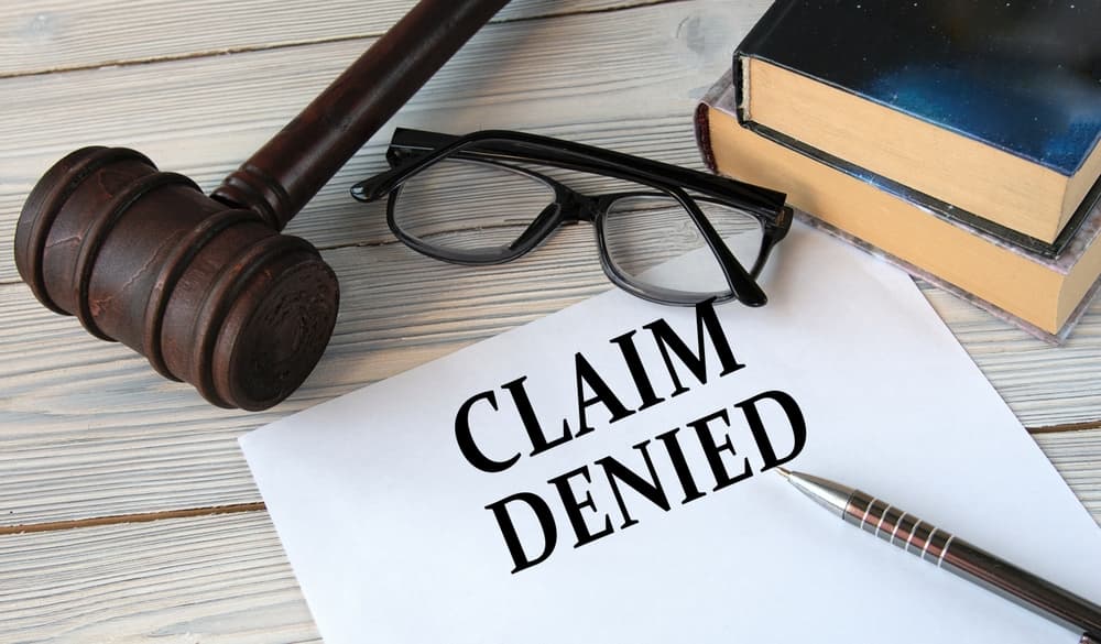 CLAIM DENIED - words on white paper with the background of the judge's hammer, glasses and pen
