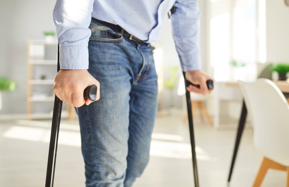 Injured man walking using his crutches at home.