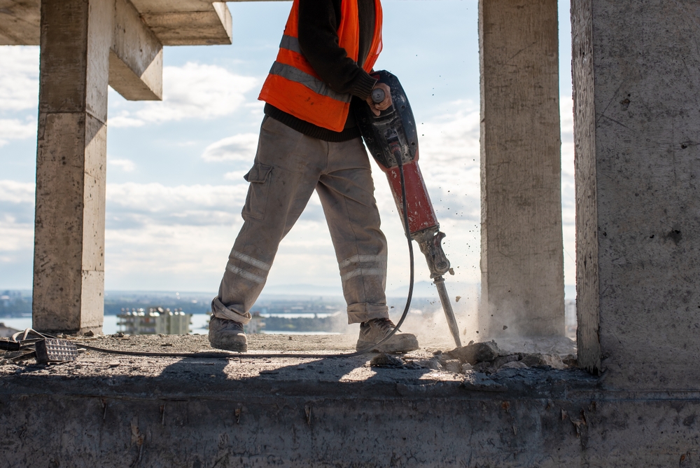 Construction worker using a jackhammer to drill into a concrete floor.