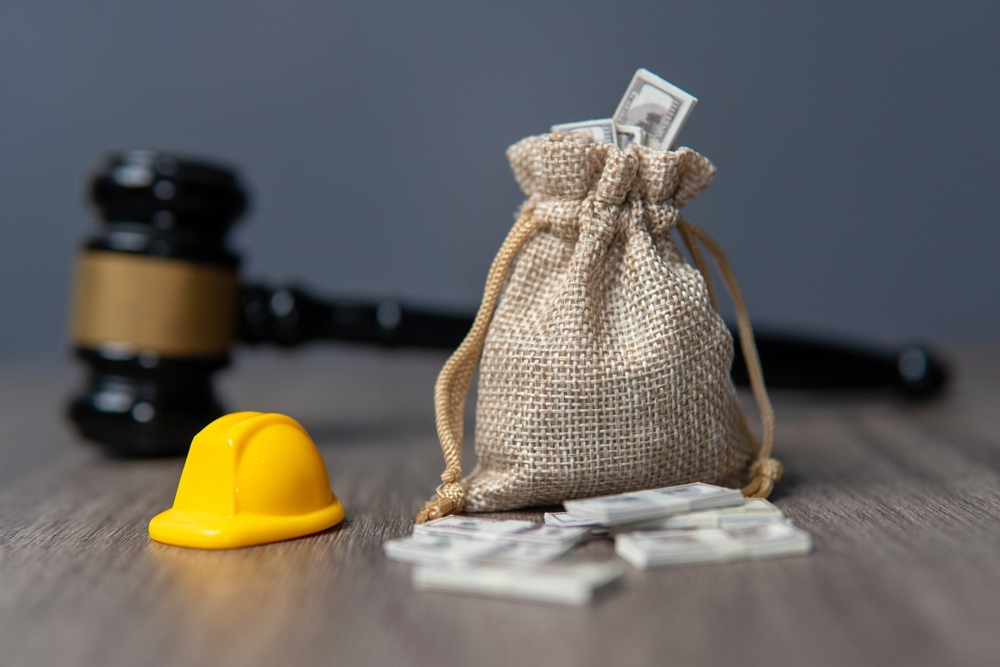 Close-up of a bag of money, a hard hat, and a gavel on a wooden table, representing Pennsylvania workers' compensation and labor law.