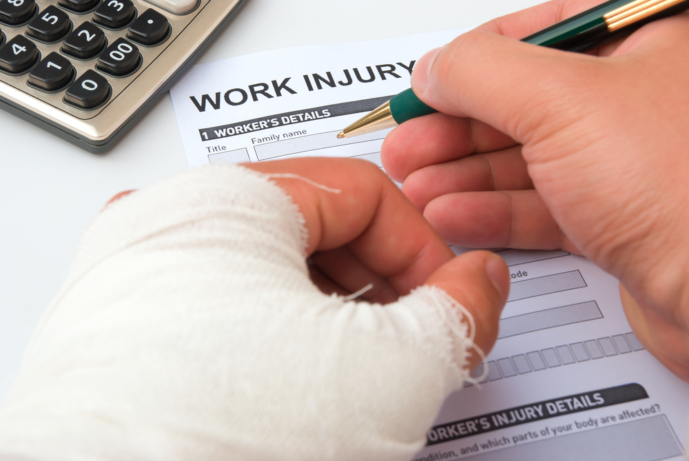 Worker with a bandaged hand filling out a work injury form at a desk.