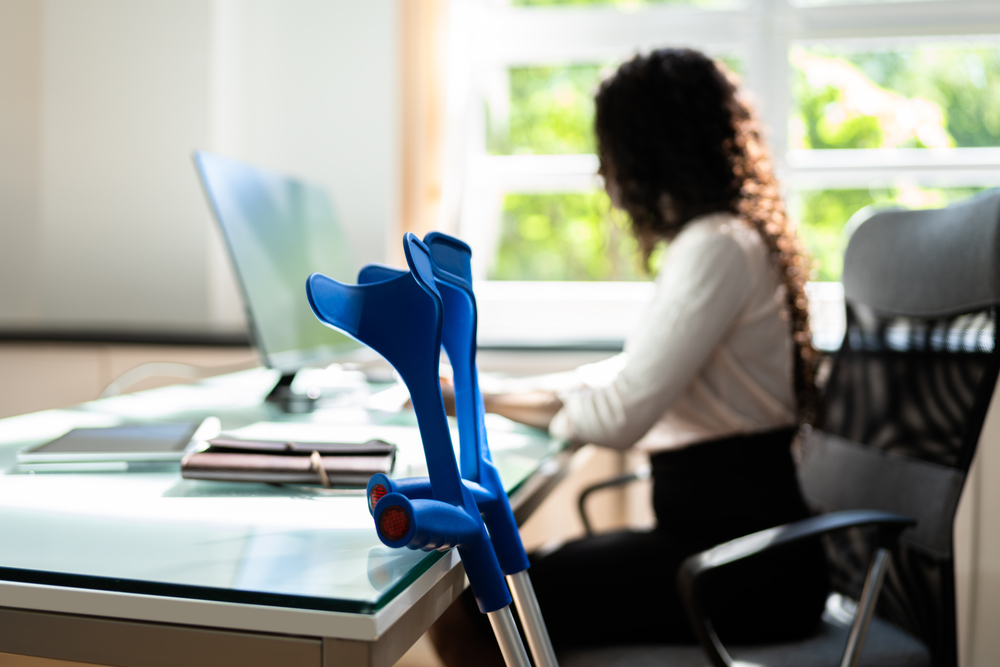 Office worker using a computer with crutches leaning against the desk.